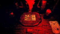A red and black table with a ram skull overlooking it, with a 'Rat King' tarot card in the table's centre